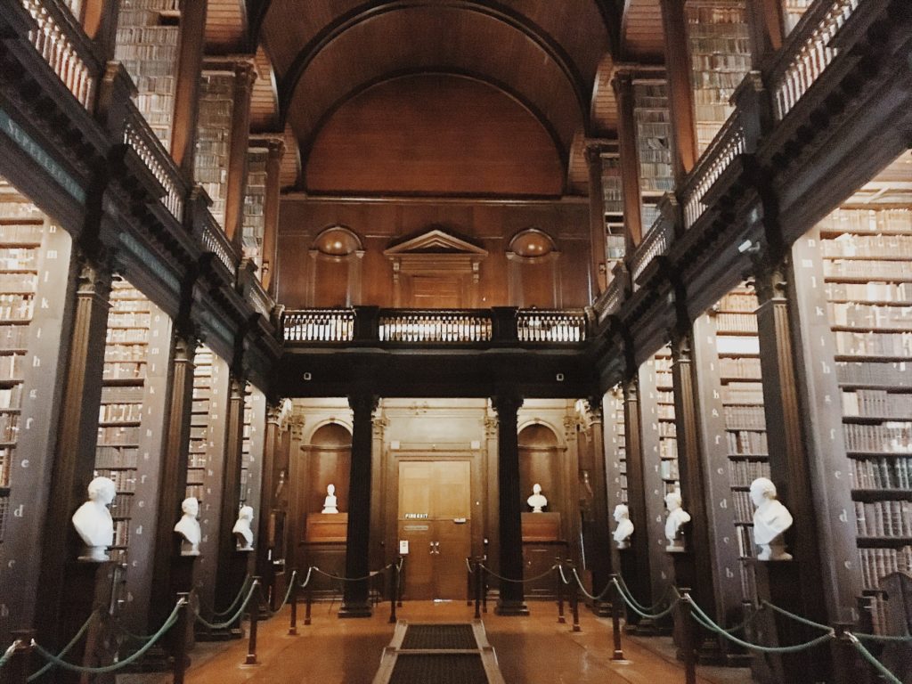 Two story wooden library with busts of famous authors along the shelves